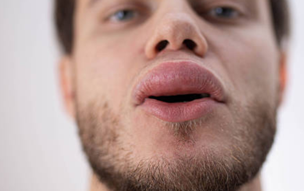Close-up of a man’s mouth with lips slightly parted and stubbly beard visible beneath.