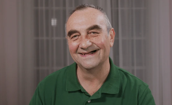 Smiling man in a green polo shirt posing indoors against a neutral background.