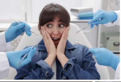 Woman at a dental clinic looking surprised as several dentists in blue gloves hold dental instruments around her mouth for a checkup.