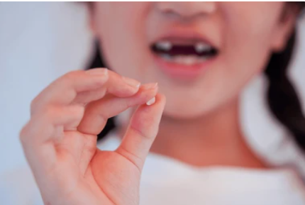 Close-up of a child’s hand pinching a tiny object near her open mouth.