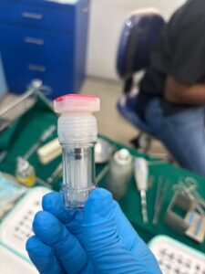 Close-up of a medical technician's gloved hands holding a small vial and syringe cap in a clinic setting.