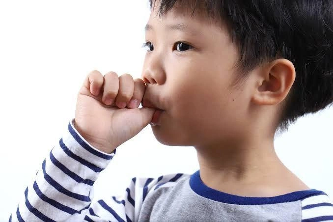 Young child in a striped shirt calmly sucking their thumb, gazing to the right.