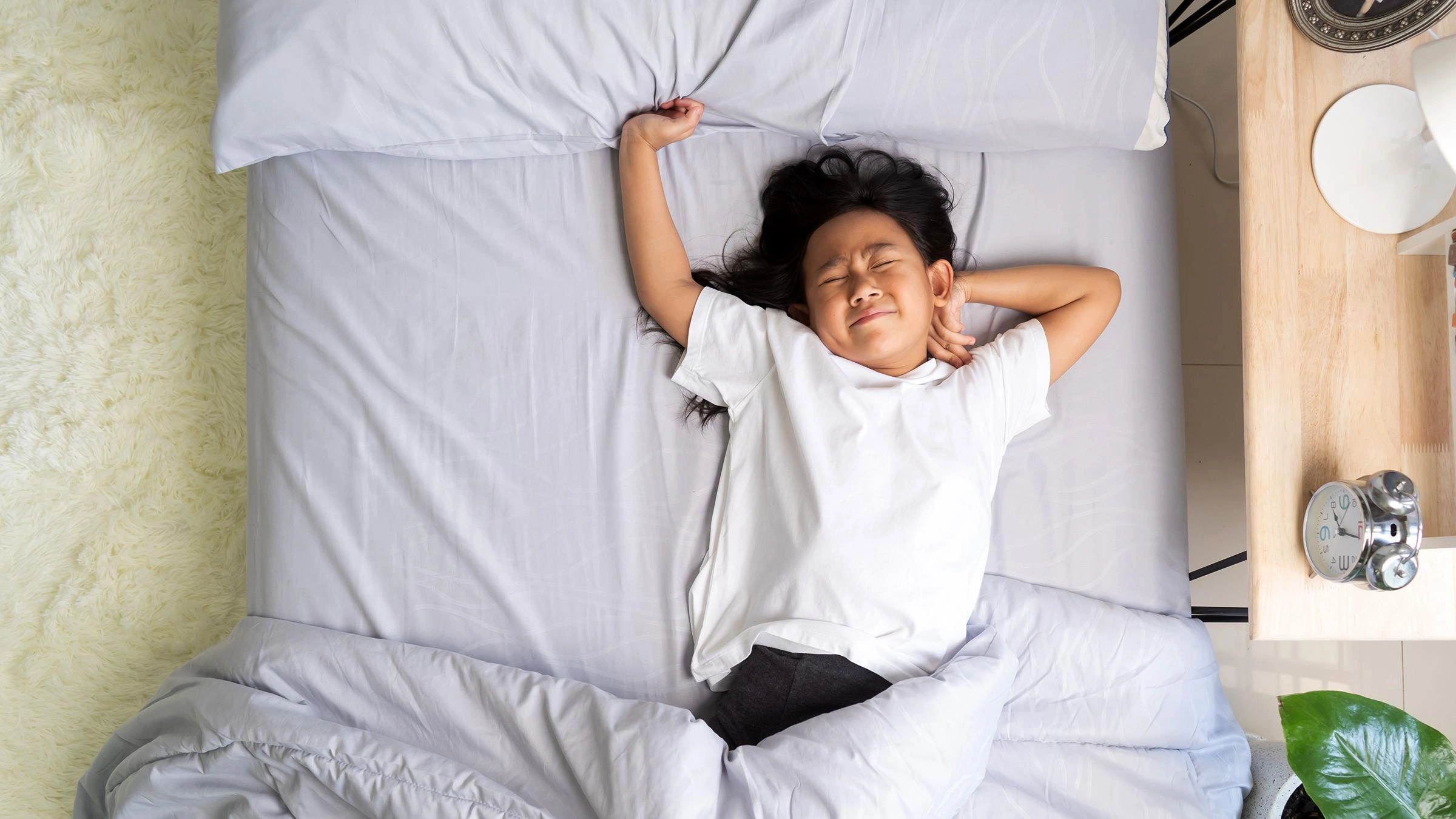 Overhead view of a child sleeping peacefully on a gray duvet, arms stretched above the head.
