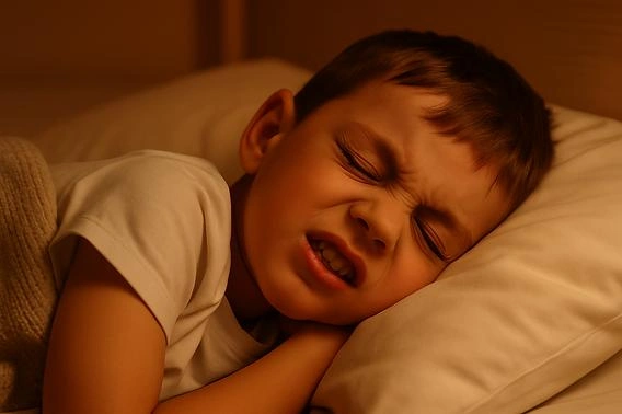 Young boy lying in bed with a pained expression, eyes tightly shut against a pillow and blanket nearby.
