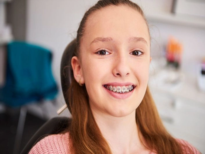 Teen girl with braces smiling in a dental chair at a clinic.